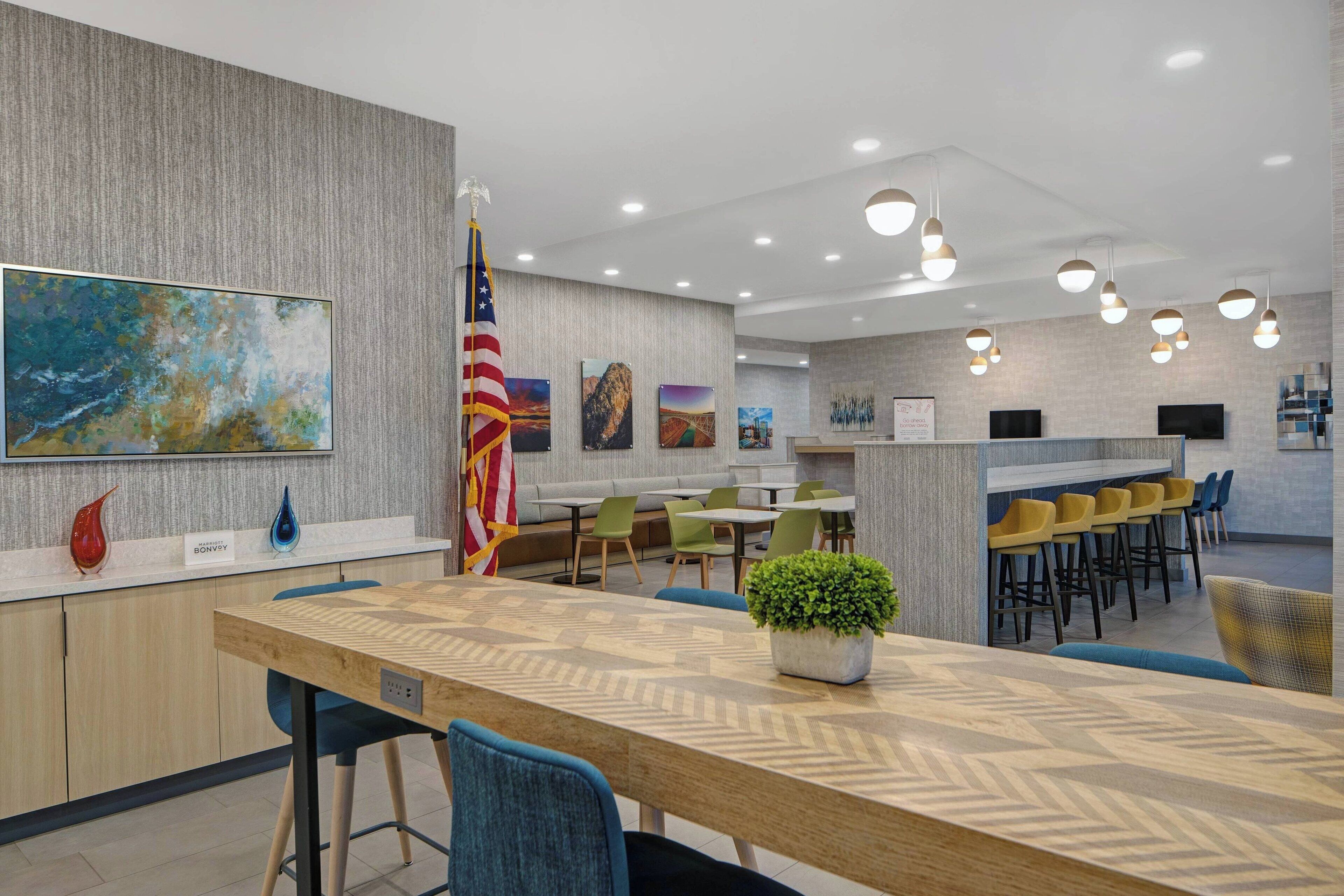 A modern hotel lobby with a long reception desk, seating area, and a bar.