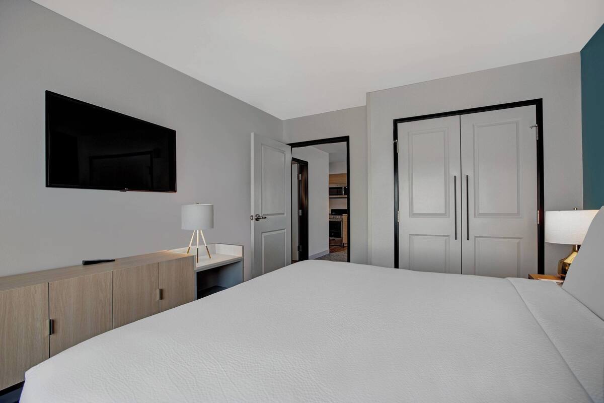 Una habitación de hotel con una cama, una mesita de noche, una lámpara, un armario y un espejo.
