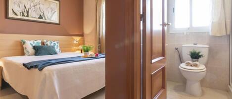 A hotel room with a bed, a painting on the wall, a toilet, and a shower area.