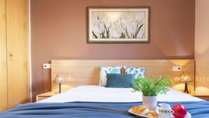 A neatly made bed with a blue blanket, a bedside table with a lamp, a framed picture of white tulips on the wall, and a tray with croissants, a mug, and a teapot on the bed. - Vacation home Lorena by Interhome (Deltebre)