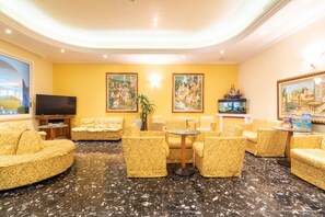 A hotel lobby with yellow patterned sofas, a flat-screen TV, framed artwork, and a decorative ship model. - Hotel Ettoral (Jesolo)