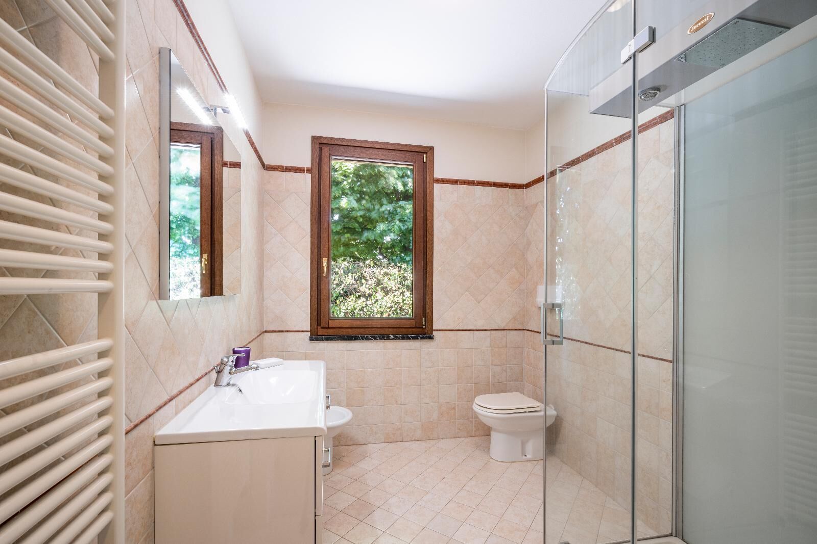 A bathroom with a window, a sink, a toilet, and a glass shower enclosure.