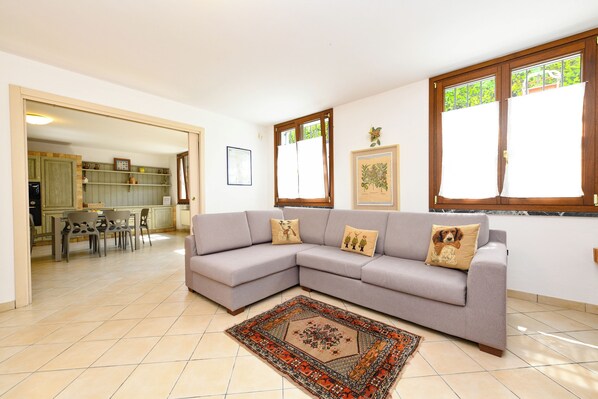 A living room with a grey sectional sofa, a patterned rug, and a dining area with chairs and a table.