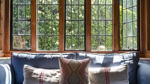 A blue sofa with patterned cushions in front of a window with a view of greenery.