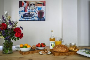 Et bord med en vase blomster, en vinflaske, et glas juice, brød og en bog.