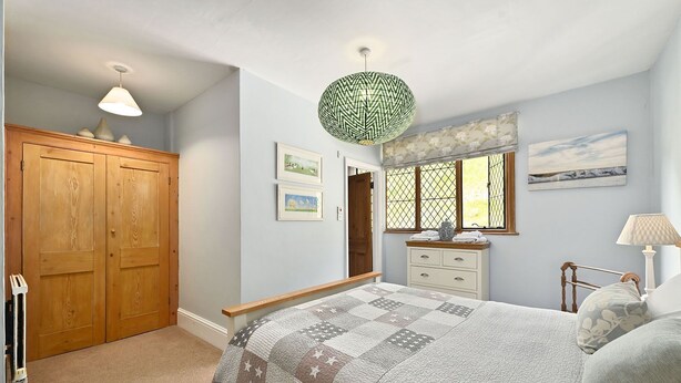 Quarto com cama, cômoda, janela com cortinas, luminária pendente e porta.
