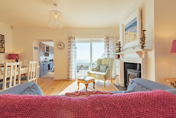 A living room with a fireplace, a dining area, and a kitchen visible through an open door.