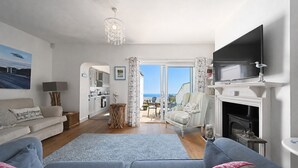 Ein Wohnzimmer mit Sofa, Fernseher, Kamin und Meerblick.
