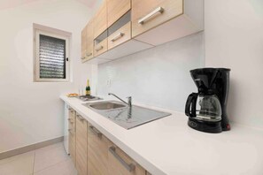 Een moderne keuken met een wit aanrecht, een roestvrijstalen spoelbak, houten keukenkastjes en een zwarte koffiezetapparaat.