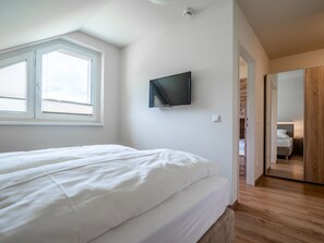 A bedroom with a bed, a television mounted on the wall, and a window with blinds. - Warm Apartment in Gosau With Shared Sauna (Gosau)