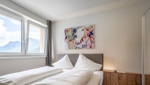 Una camera d'albergo con un letto, una finestra vista montagna e un quadro appeso al muro.