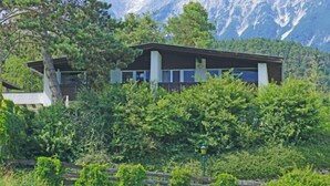 A modern building with a flat roof, surrounded by dense greenery and mountains in the background. - Chalet St. Wendelin - Typ B by Interhome (Telfs)