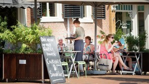 An outdoor cafe with tables and chairs, a chalkboard menu, and a brick building in the background. - Traditional Villa in Tzummarum near Sea (Tzummarum)