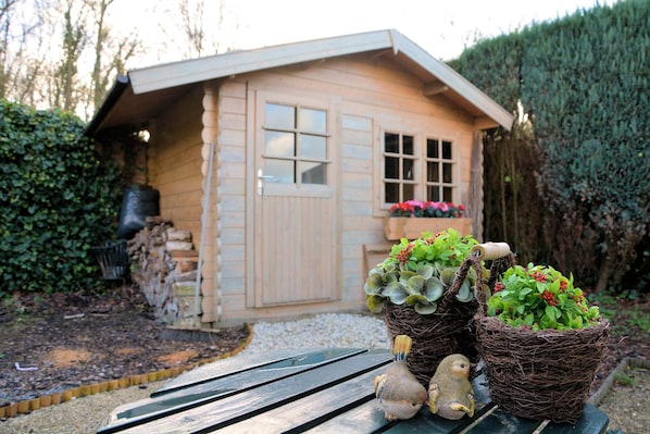 A wooden cabin with a window, a door, and a small garden area with potted plants and a bird figurine.