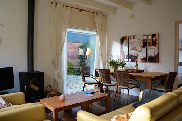 Un salon comprenant un canapé, une table en bois, des chaises en osier, une cheminée et un coin repas avec une table et des chaises.
