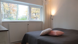 Et soveværelse med seng, et vindue, en radiator og en vægmonteret lampe.