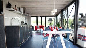 A modern kitchen with white cabinets, a dining area with blue chairs, and a large window with a view of the outdoors. - Modern, Trendy F1 Theme Lodge, Near the Sea (Zandvoort)