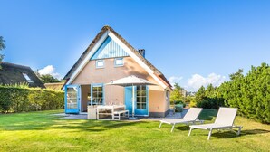 A house with a sloped roof, a patio with a table and chairs, and a lawn with two lounge chairs. - Holiday Home on Texel With Spacious Garden (De Koog)