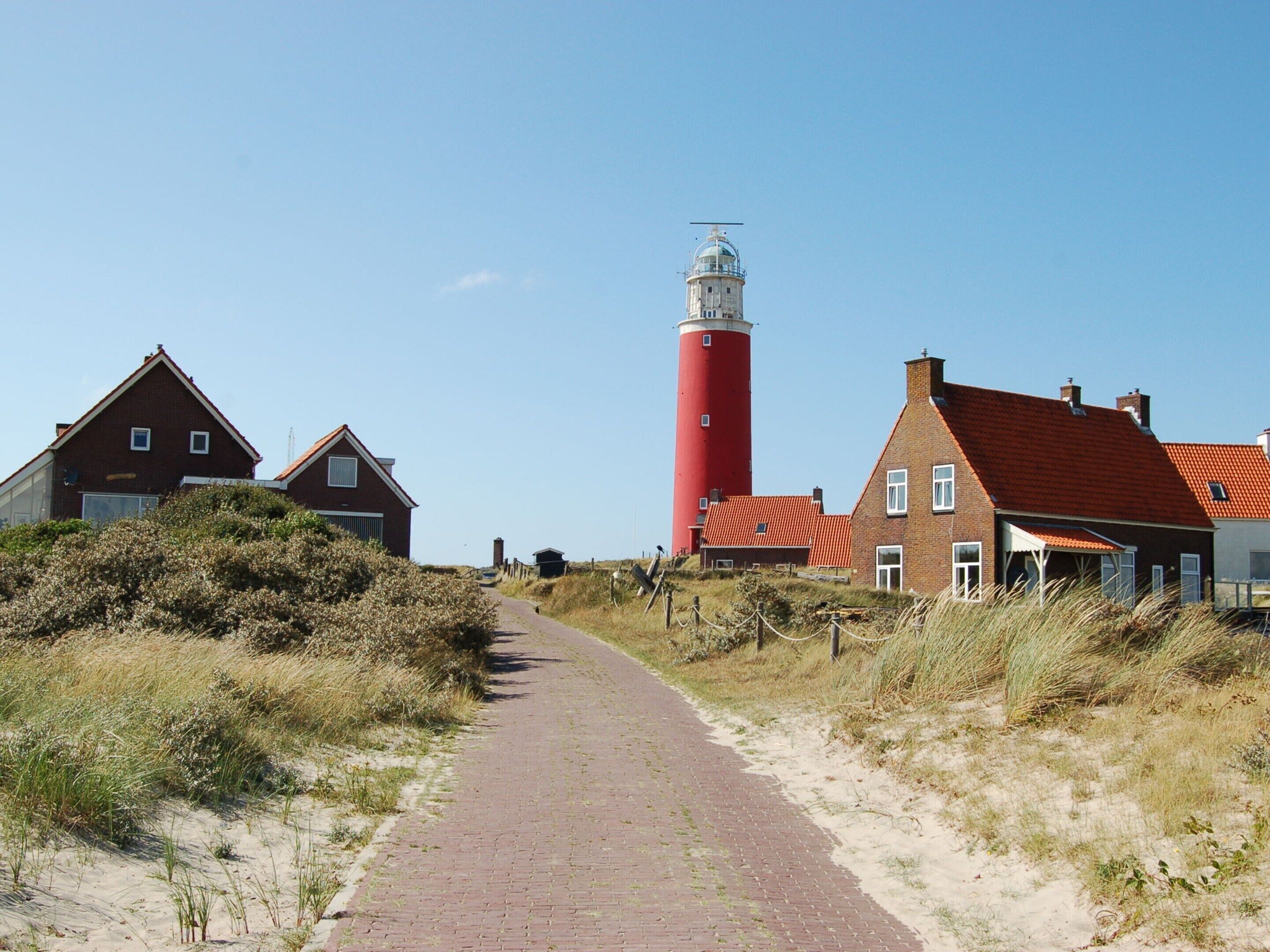 Ein Küstenpfad führt zu traditionellen Häusern mit roten Dächern und einem roten Leuchtturm.