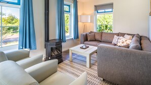 A modern living room with a sofa, armchairs, a coffee table, and a wood-burning stove. - Holiday Home on Texel With Spacious Garden (De Koog)