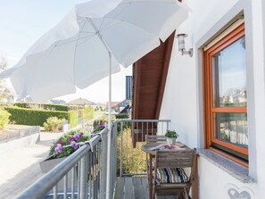 Un balcon avec une table en bois, des chaises, une plante en pot et un grand parasol blanc.