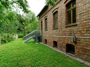 Traditional brick building with a central entrance and staircase, set amidst a serene natural setting with trees and shrubs.