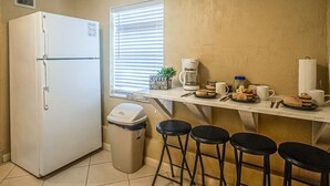 Une cuisine avec un réfrigérateur blanc, un coin café et quatre tabourets noirs.