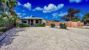 Une maison avec une allée en gravier, une cour clôturée et un ciel bleu dégagé.