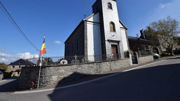A church with a tall steeple and a flagpole with a flag. - Beautiful Cottage in Malempre With Fenced Garden (Manhay)