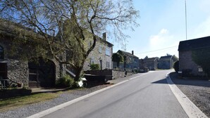 A quiet, tree-lined street with stone buildings, a clear sky, and a gravel driveway. - Beautiful Cottage in Malempre With Fenced Garden (Manhay)