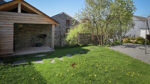 A stone house with a wooden porch, a swing set, and a tree in the yard. - Beautiful Cottage in Malempre With Fenced Garden (Manhay)
