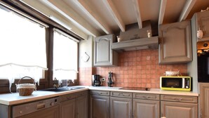 A kitchen with grey cabinets, a tiled backsplash, a microwave, and a window with a basket on the counter. - Beautiful Cottage in Malempre With Fenced Garden (Manhay)