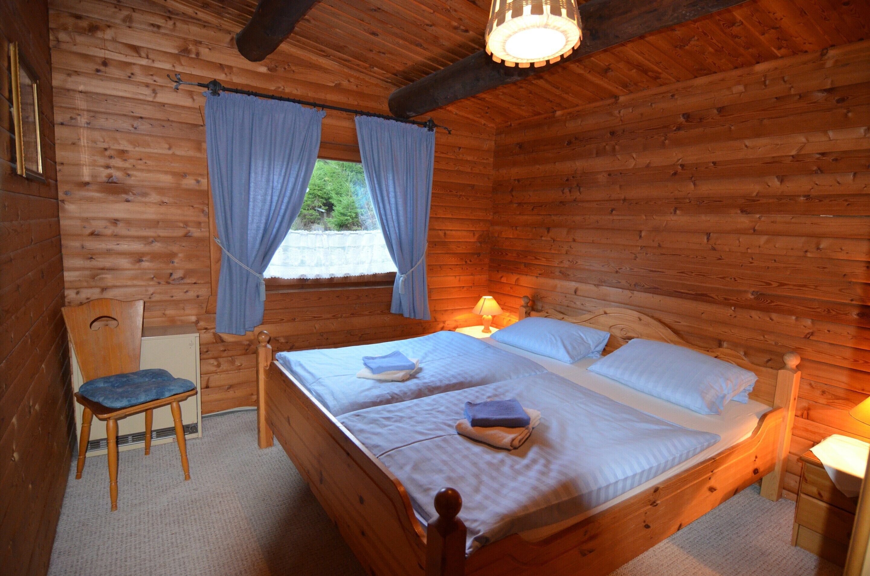 Een slaapkamer in een houten chalet met een tweepersoonsbed, een stoel en een bijzettafeltje.