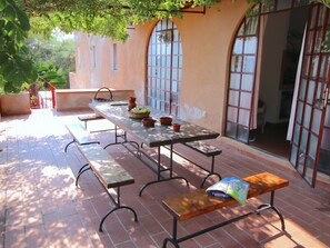 An outdoor patio with a long table and benches, surrounded by a brick floor and large windows. - Mansion in Capo Vaticano by the Sea (Ricadi)