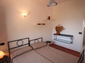 A bedroom with a bed, bedside lamp, shelves with decorative items, and a hanging light fixture. - Mansion in Capo Vaticano by the Sea (Ricadi)