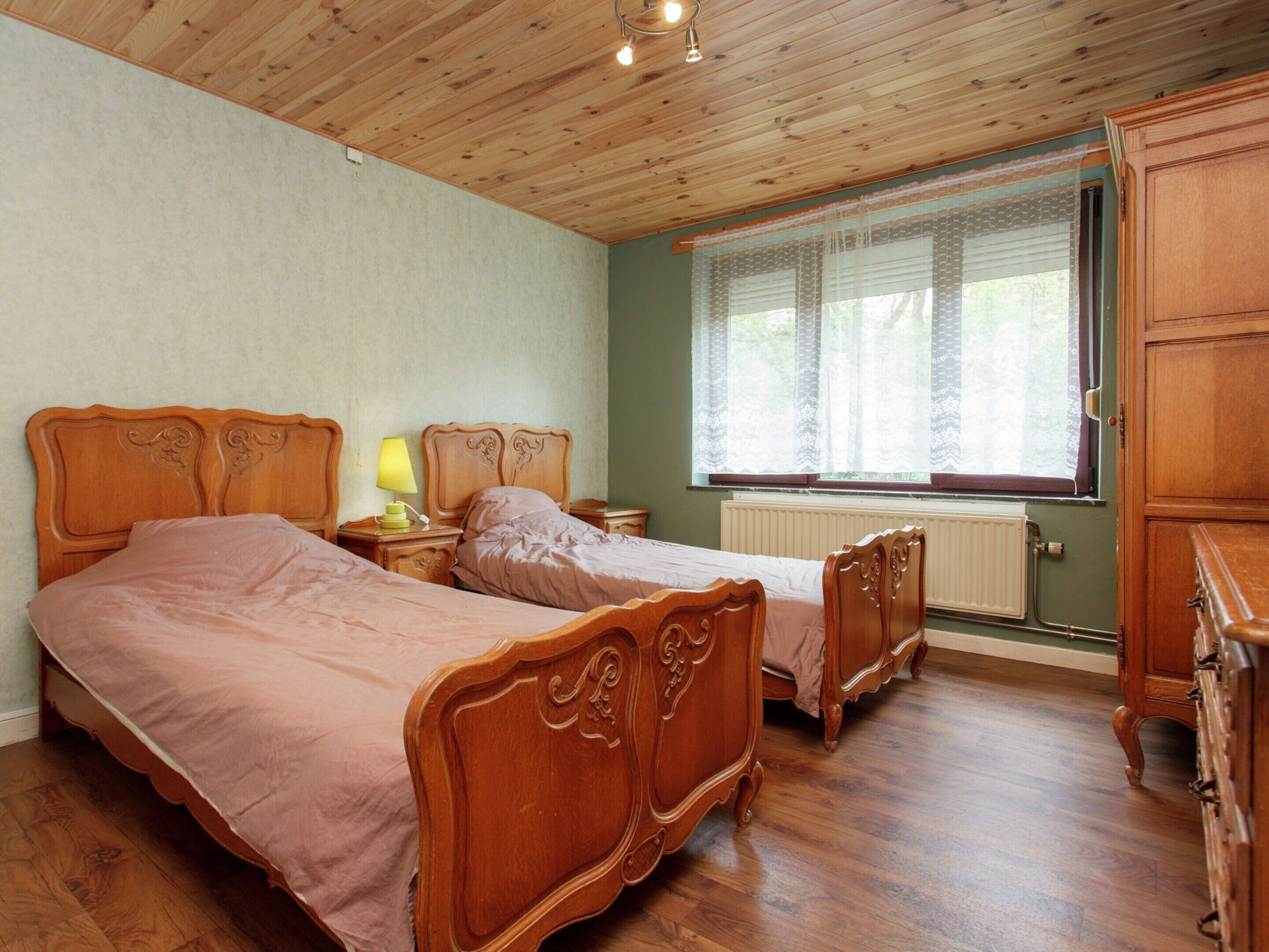 A bedroom with two wooden beds, a nightstand with a lamp, a dresser, and a window with blinds.
