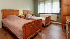 A bedroom with two wooden beds, a nightstand with a lamp, a dresser, and a window with blinds. - Quaint Holiday Home With Fenced Garden in Manhay (Manhay)