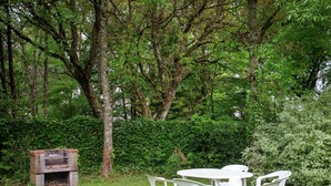 A garden with a stone barbecue, white plastic chairs, and a table. - Quaint Holiday Home With Fenced Garden in Manhay (Manhay)