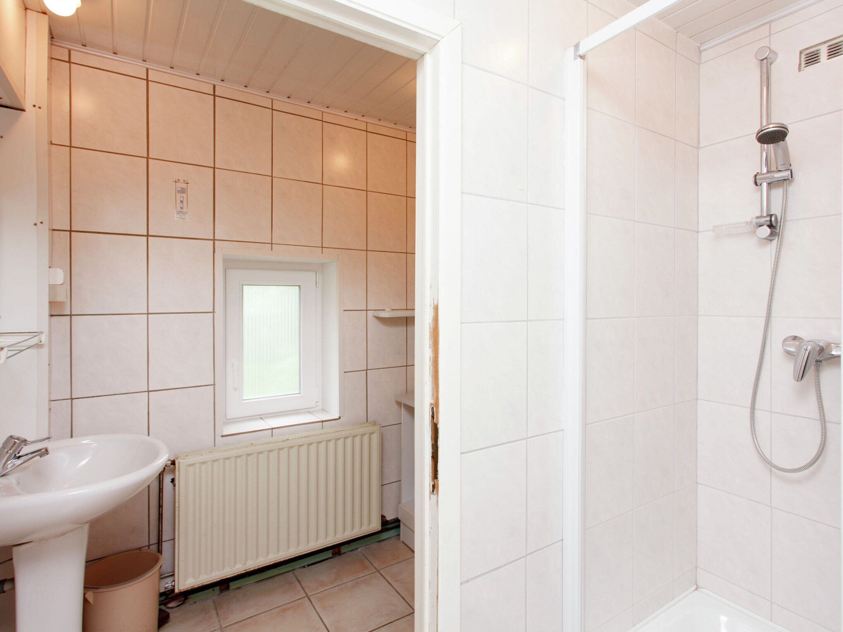 A bathroom with a white sink, a window, a shower, and a radiator.