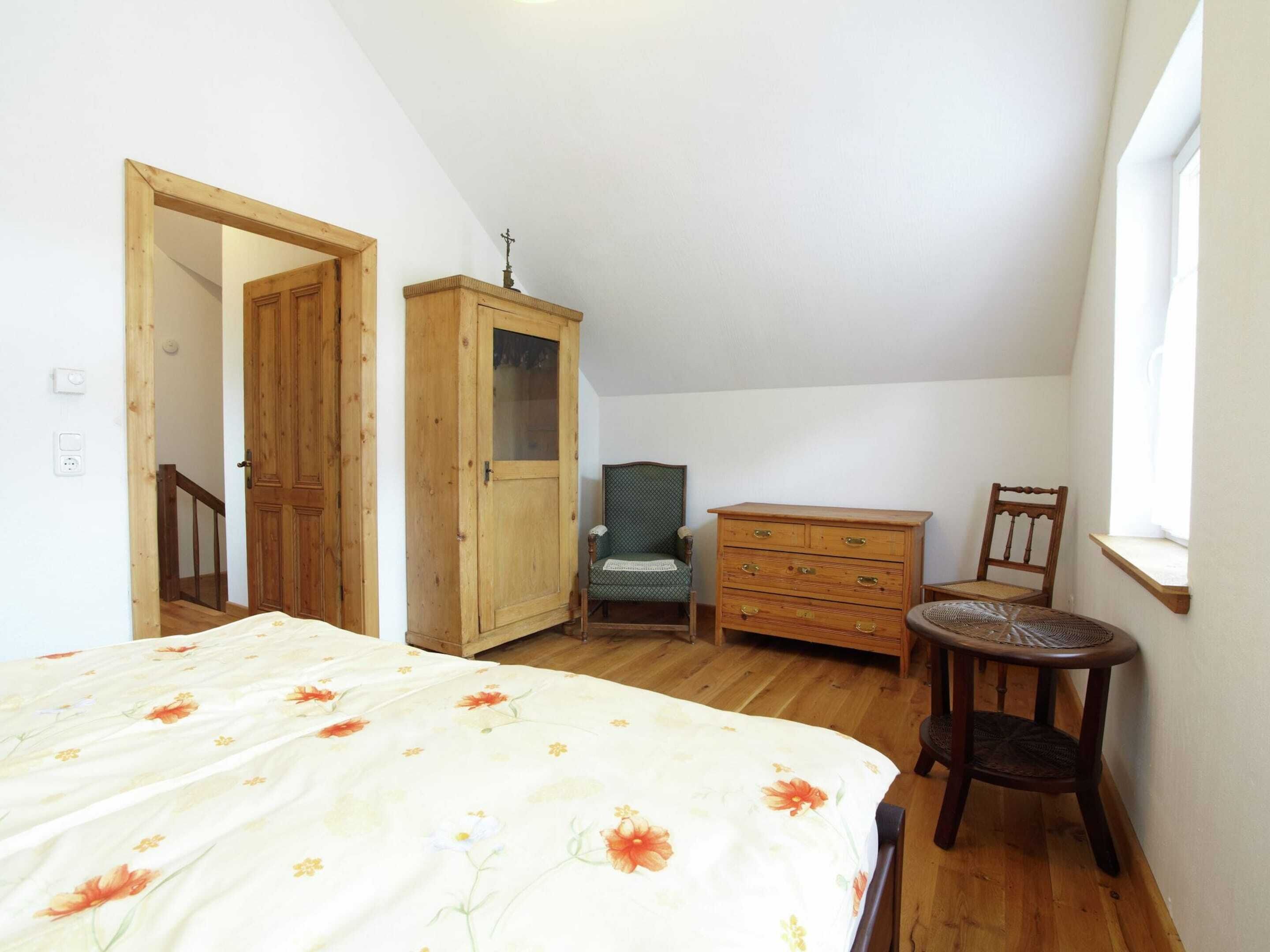Un dormitorio con cama, un armario de madera, una silla, una mesita y un ventanal.