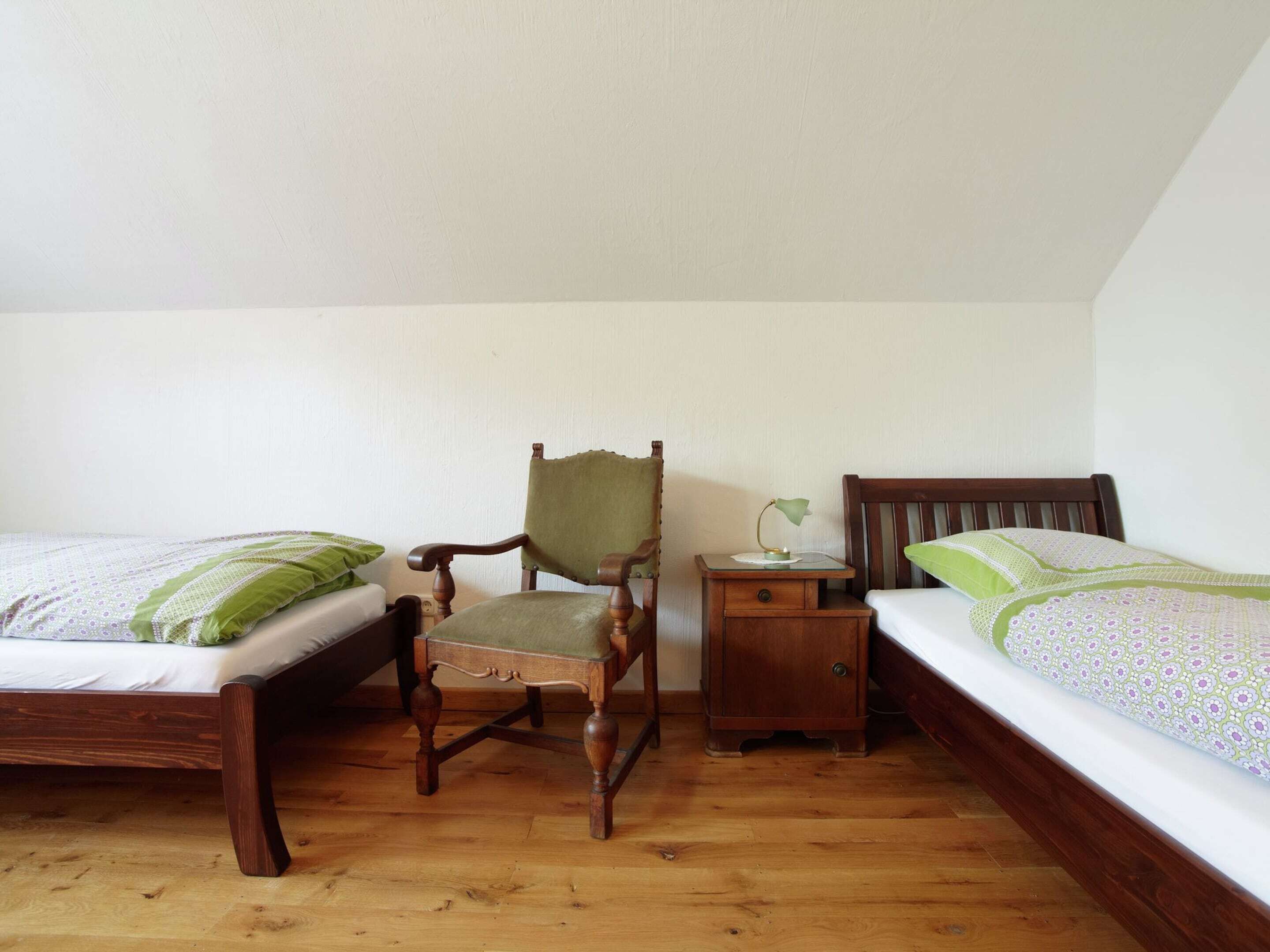 Un dormitorio con dos camas individuales, una silla de madera, una mesita de noche y una lámpara.