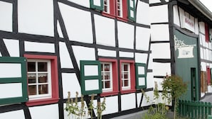 A traditional half-timbered building with red and green window shutters, a green door, and a sign indicating a restaurant. - Nostalgic Apartment in the Beautiful Eifel Region (Schleiden)