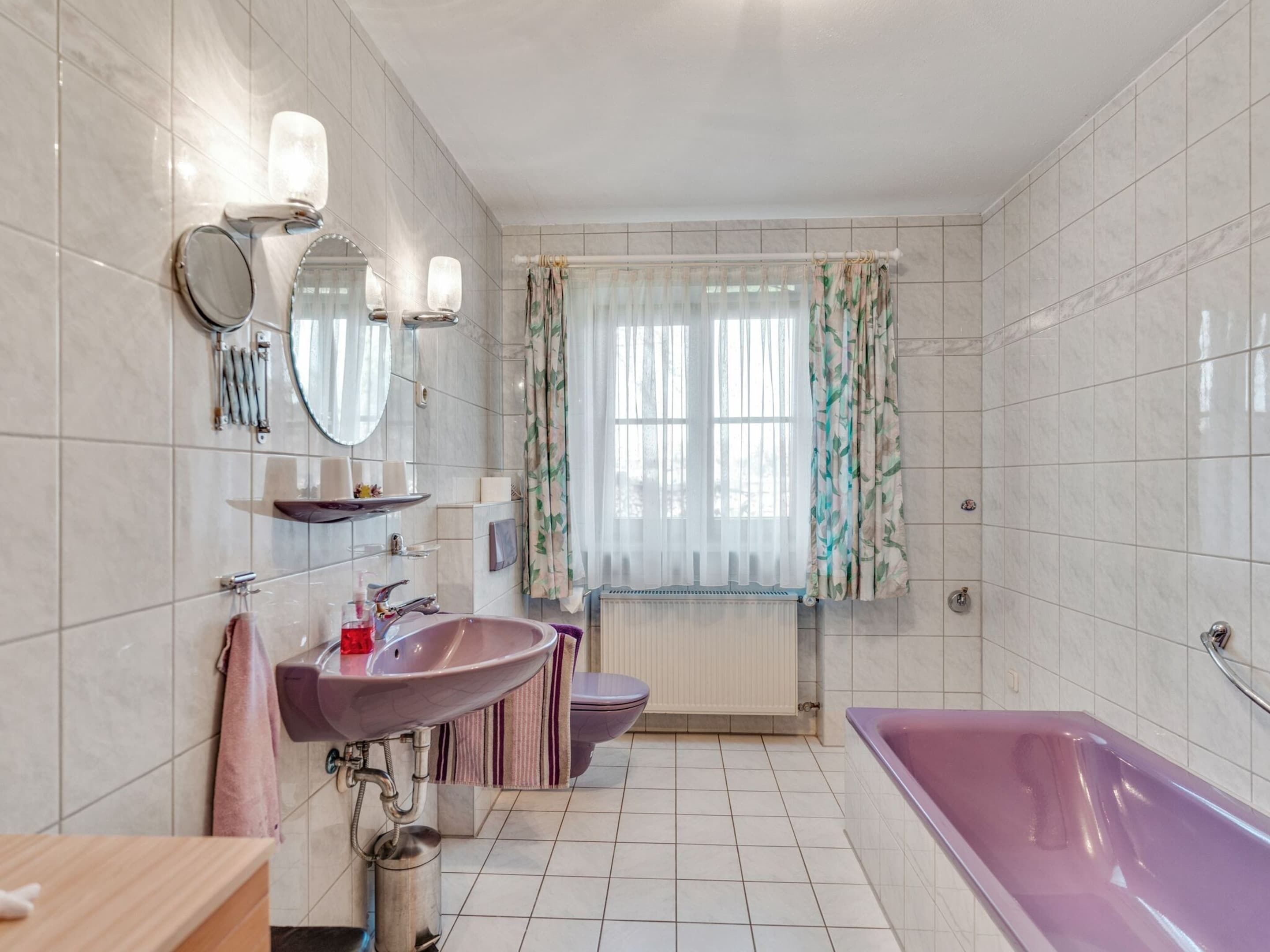 A bathroom with a large bathtub, a sink, a toilet, and a window with curtains.