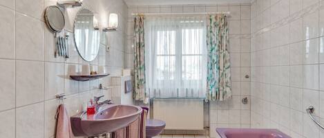 A bathroom with a large bathtub, a sink, a toilet, and a window with curtains.