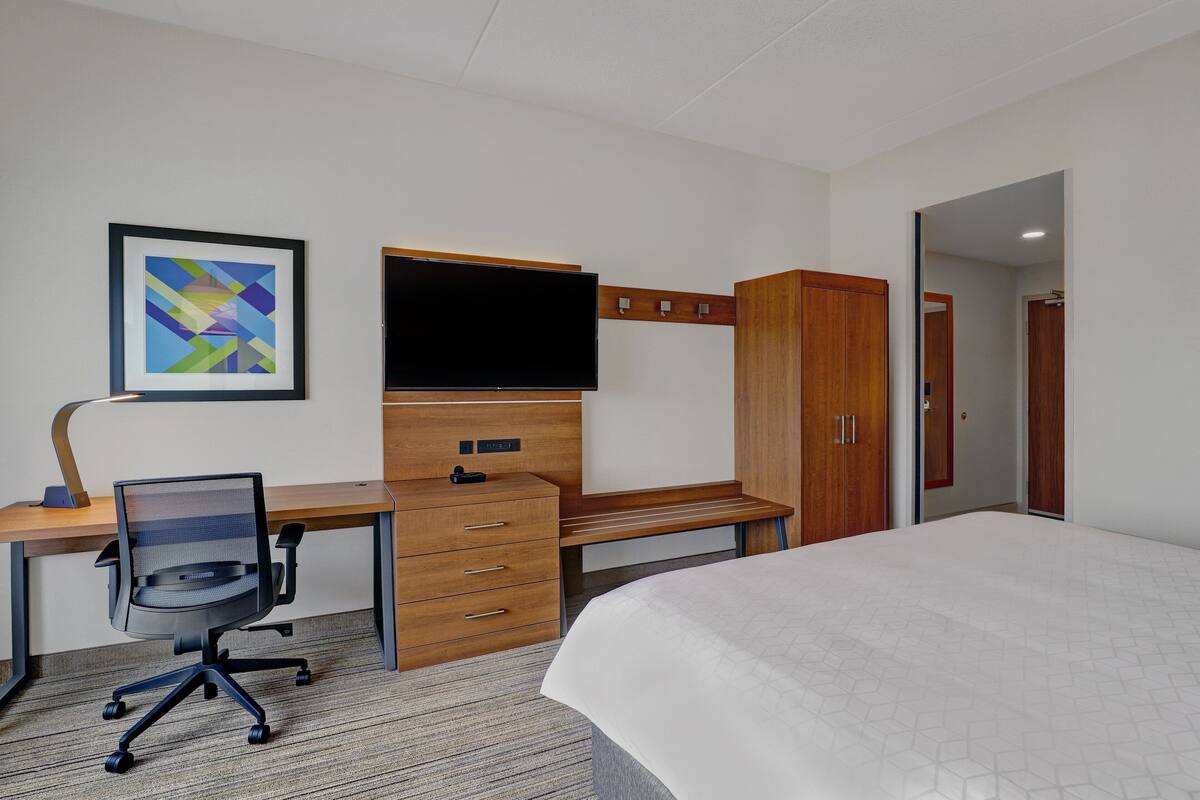 Une chambre d’hôtel équipée d’un lit, d’un bureau avec un ordinateur, d’une chaise, d’une télévision et d’une armoire.