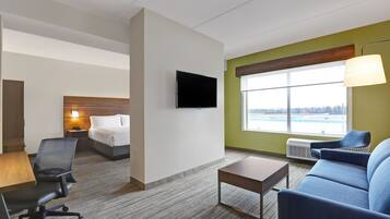 Ein Hotelzimmer mit Bett, Schreibtisch, Stuhl, Sofa, Fernseher und einem Fenster mit Aussicht.