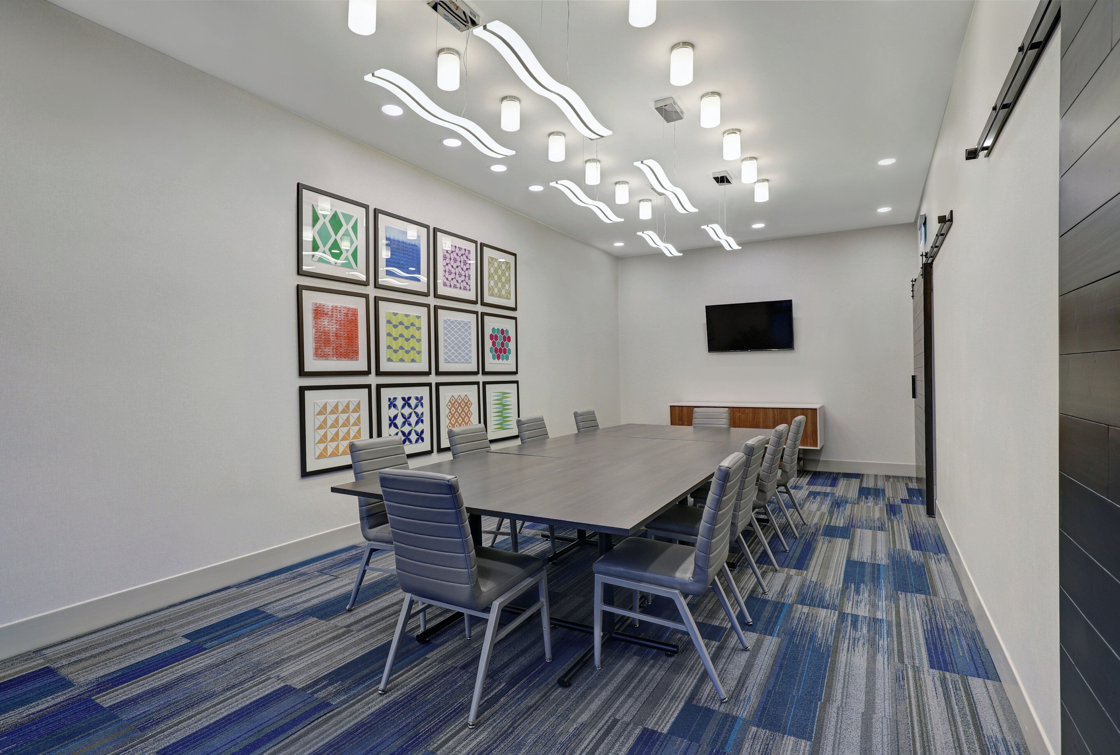 A conference room with a long table, chairs, a flat-screen TV, and framed artwork on the wall.