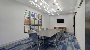 A conference room with a long table, chairs, a flat-screen TV, and framed artwork on the wall.