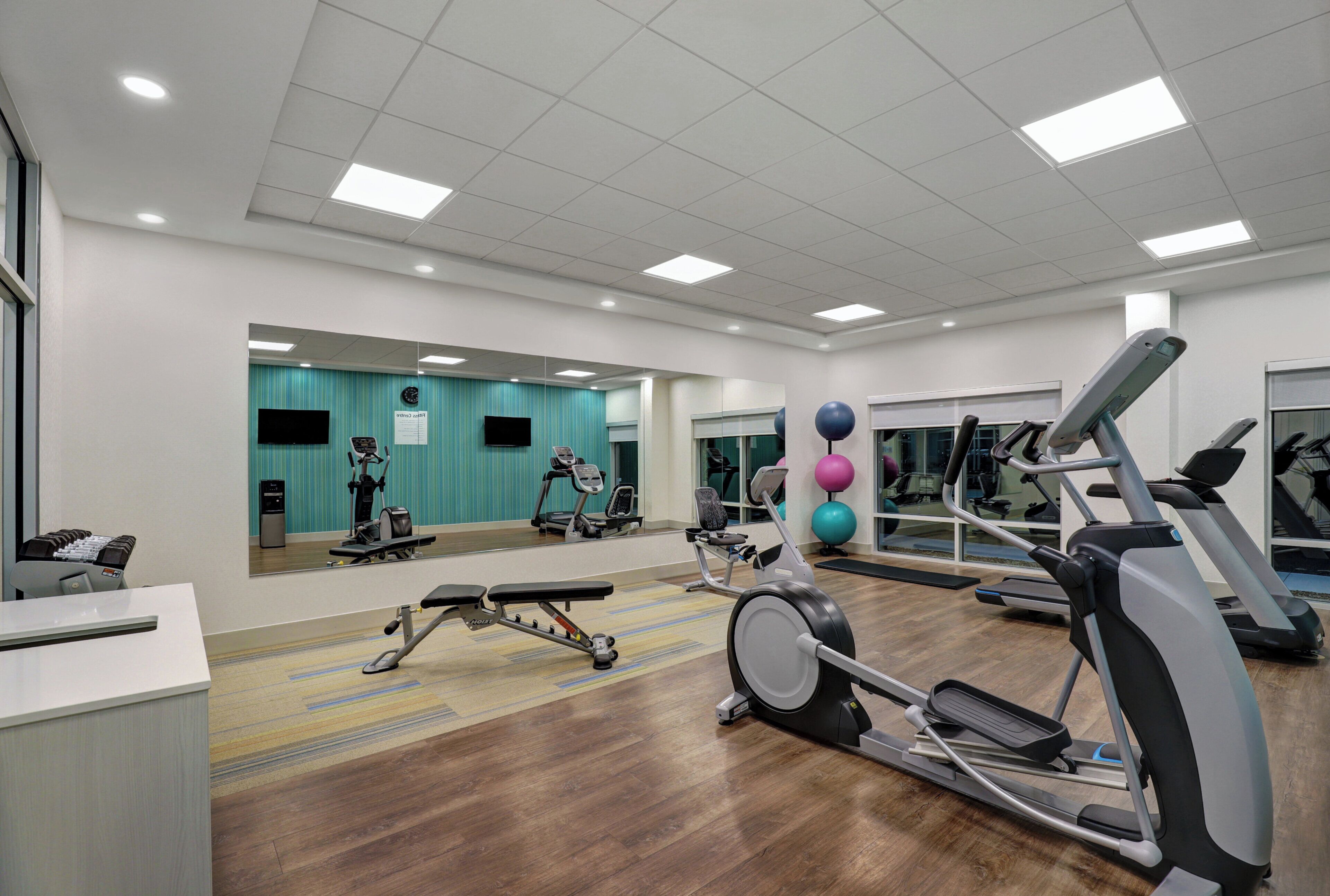 Una palestra con diverse attrezzature per esercizi, uno specchio e un pavimento in legno.