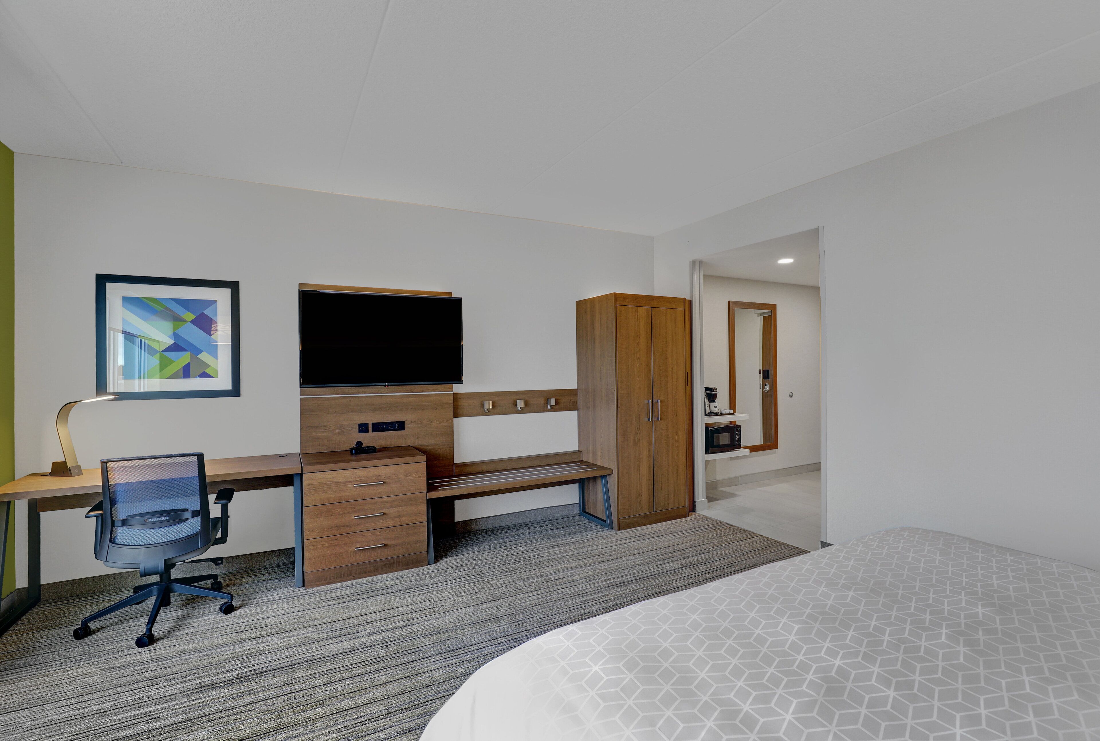 Una habitación de hotel con cama, escritorio, silla, armario y televisor.